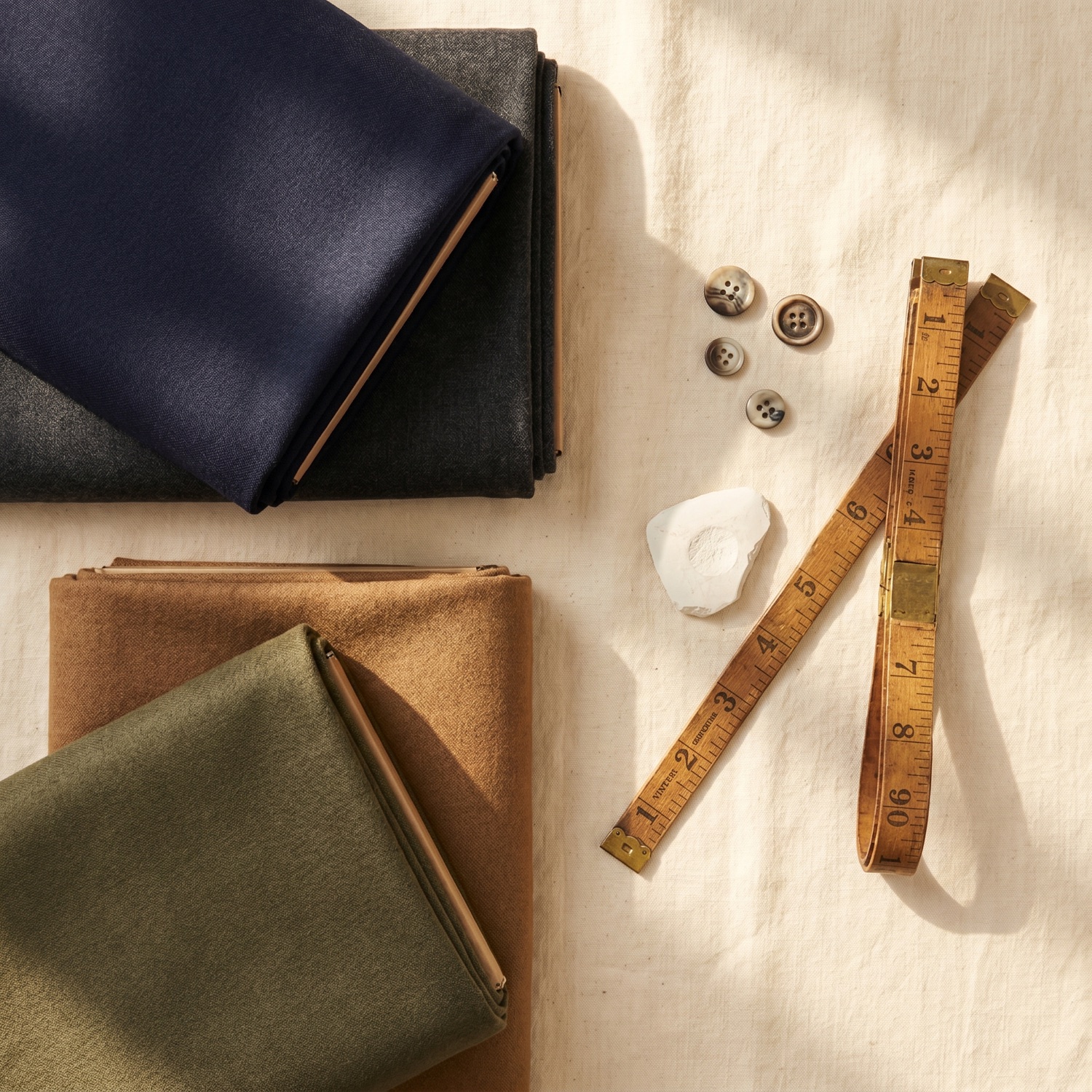 Folded premium European suiting wool in navy, charcoal, tan and olive with horn buttons, tailor's chalk and a measuring tape